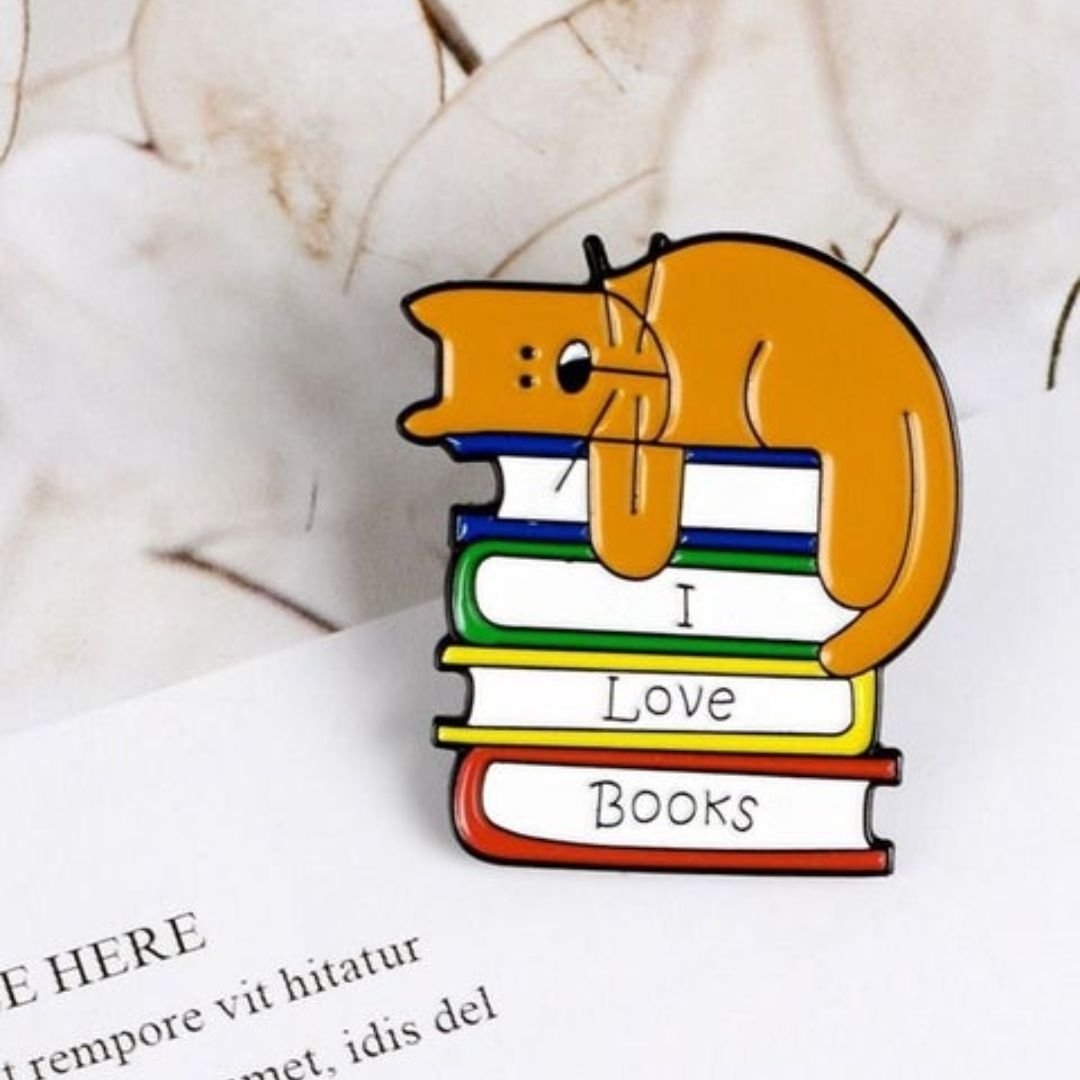 I Love Books cat enamel pin with ginger cat sleeping on colourful stack of books