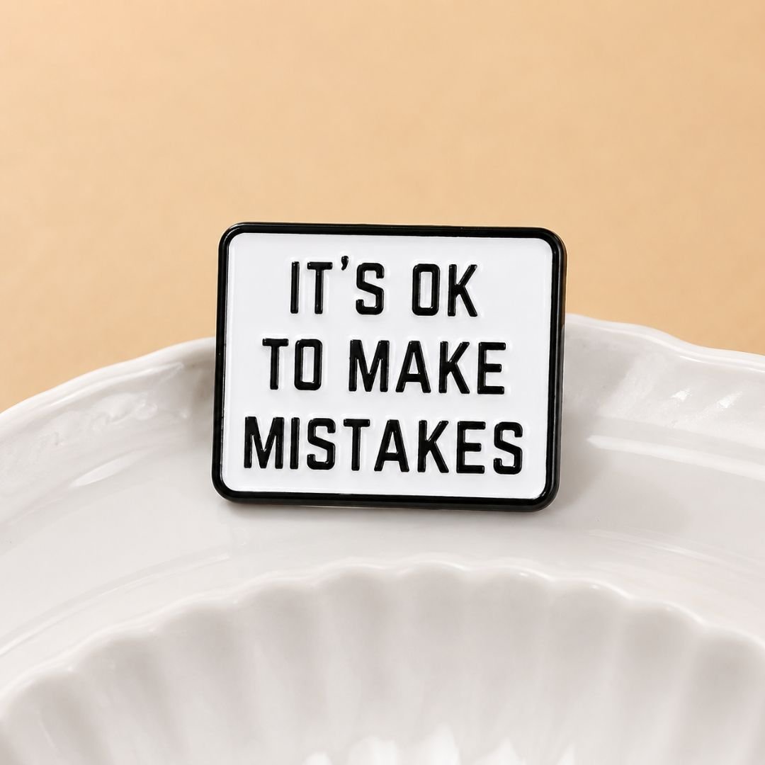 It's ok to make mistakes enamel pin standing in white ceramic dish lifestyle motivational lapel pin amber background