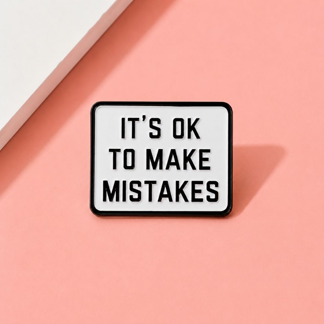 It's ok to make mistakes enamel pin pink flat lay lifestyle motivational lapel pin on pink background