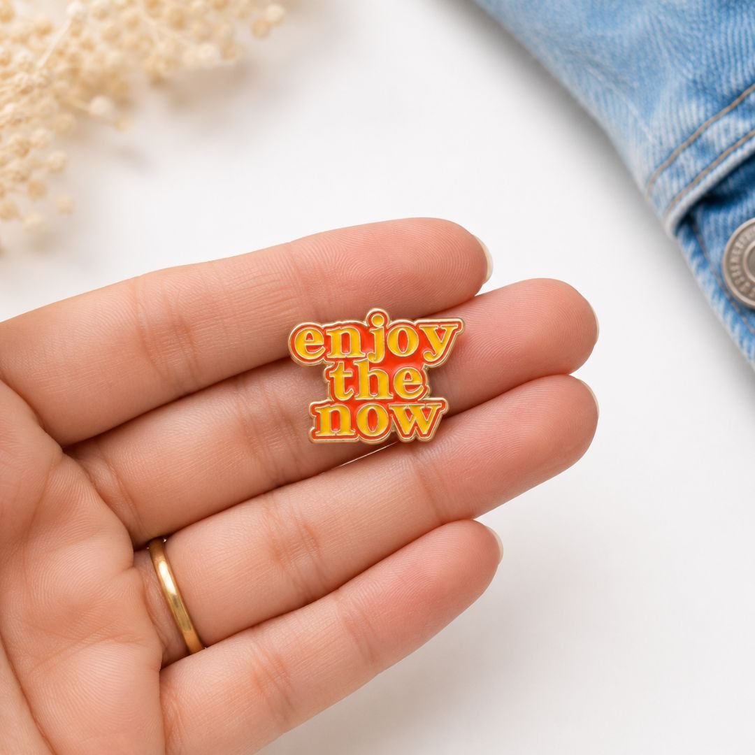 Enjoy the Now hard enamel lapel pin with retro motivational typography for jackets, backpacks and everyday accessories.