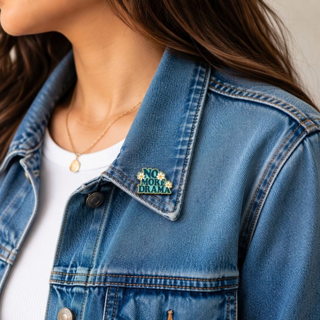 No More Drama hard enamel lapel pin with retro typography and daisy flowers on a denim jacket.